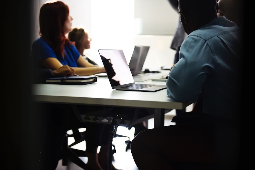 Two women and two men in a meeting. Some have laptops on the table in front of them.