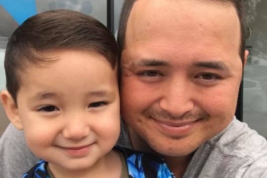 A toddler with dark brown hair with his dad, whose hair is receding. Both a smiling widely in this selfie
