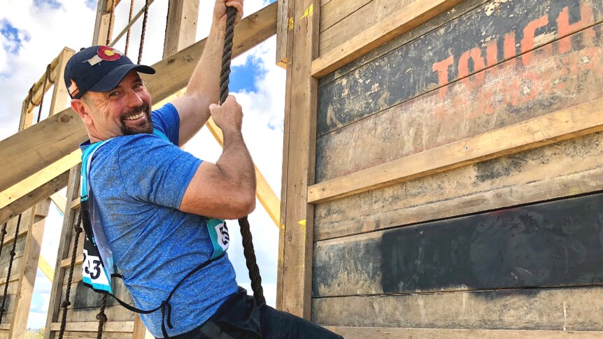 Man holding onto a rope climbing up a wall. He's smiling.
