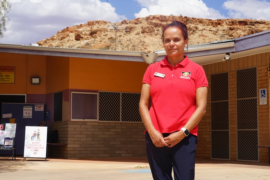 Geraldine Dennis stands in front of a health clinic with a rock formation in the background.