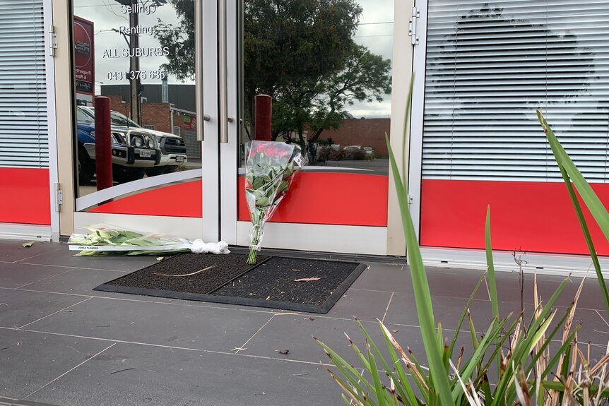A bunch of red roses on the ground outside a business office.