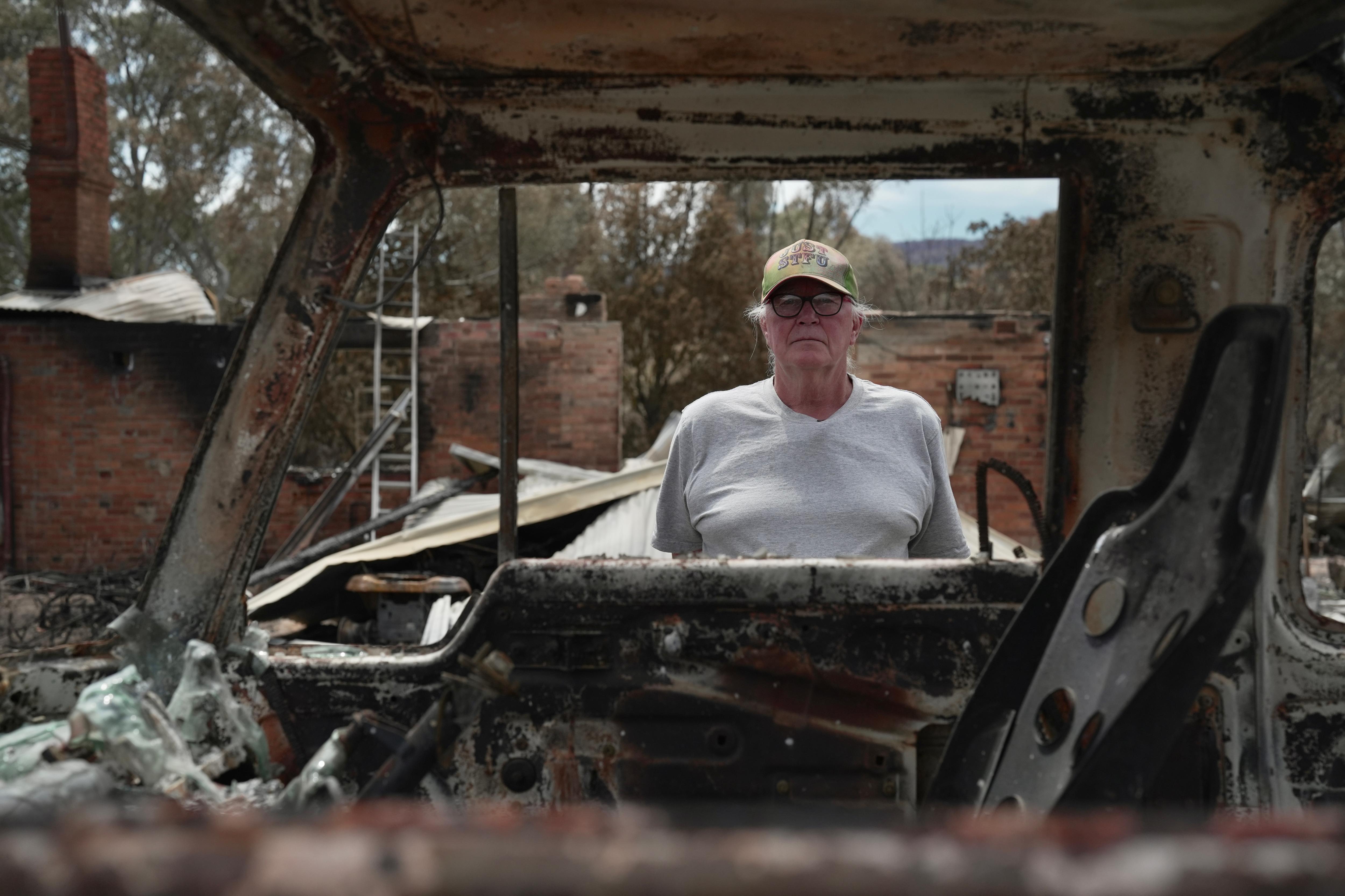 Olhando pela janela de um veículo incendiado está um homem de camiseta branca e boné de beisebol verde.