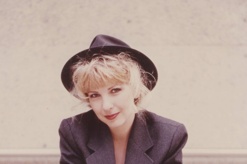 Lori Balmer poses in a promotional image from the 1990's wearing a suit jacket and fedora.