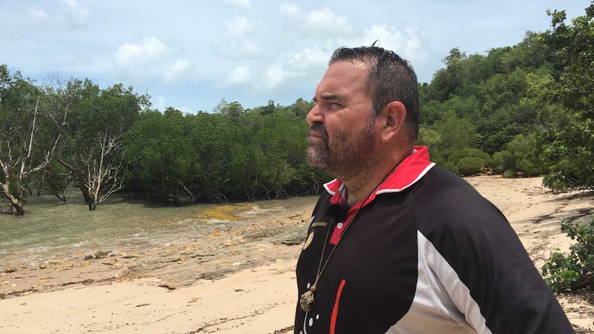 A man standing on a beach looking off-camera.