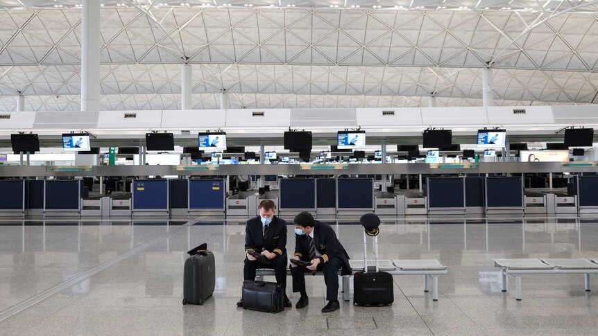 Two pilots in face masks sit in an empty terminal