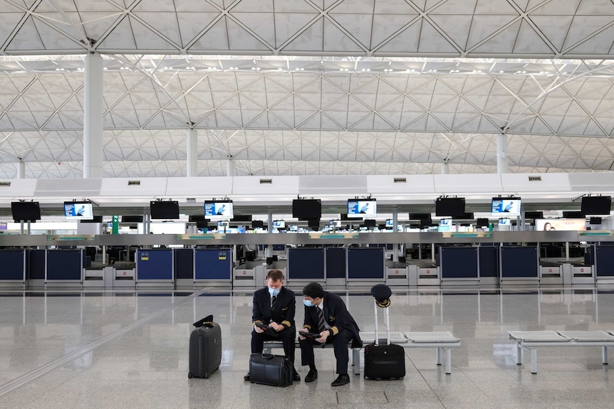 Two pilots in face masks sit in an empty terminal