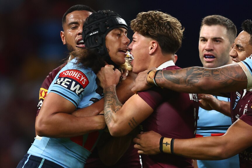 One NSW and one Queensland State of Origin player grab each others' jerseys as they face off in the middle of a game. 