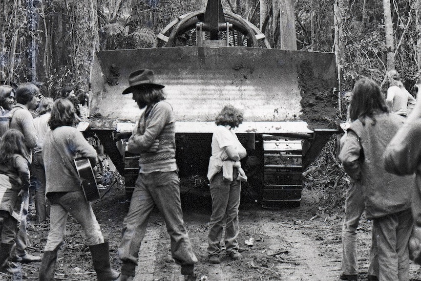 Black and white image of several protesters standing in front of a bulldozer in a rainforest.