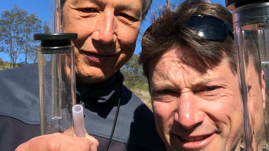 A selfie of two men holding glass tubes. The glass tubes are used to catch grasshoppers