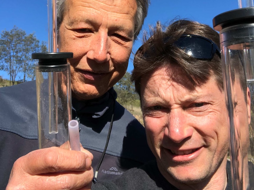 A selfie of two men holding glass tubes. The glass tubes are used to catch grasshoppers