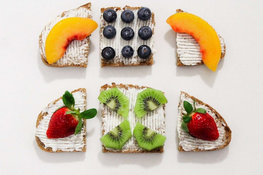 Three sliced pieces of toast with cream cheese, berries, peaches and kiwi fruit.