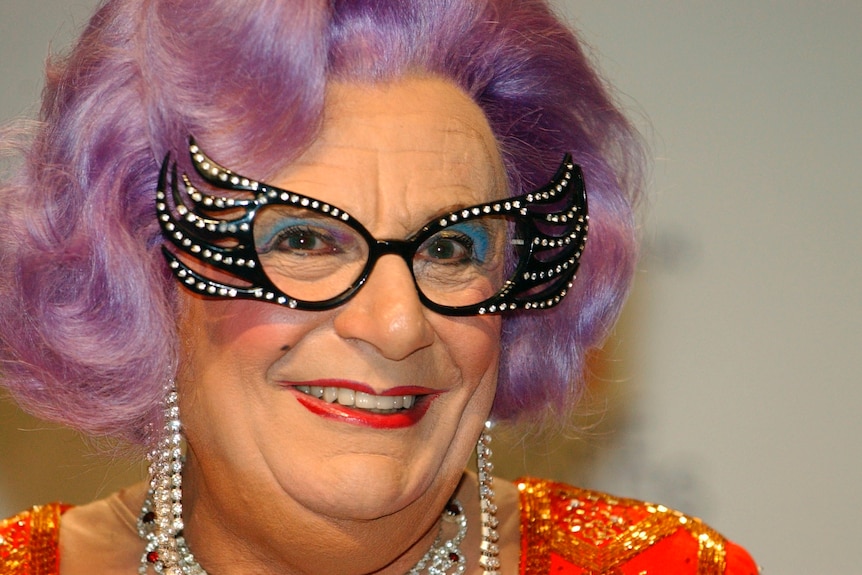 A close-up image of Dame Edna Everage, a character of Barry Humphries, with a purple wig and flamboyant glasses.