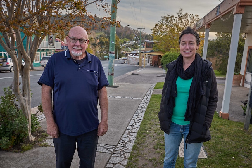 A man and woman stand side by side on a street, looking into the camera.