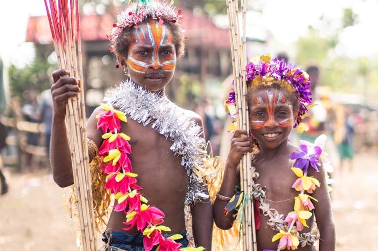 A portrait of two children wearing grass skirts and garlands of flowers.
