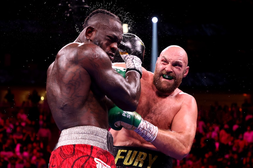 Tyson Fury hace una mueca mientras golpea a Deontay Wilder en la cabeza, con sudor rociando la cabeza de Wilder