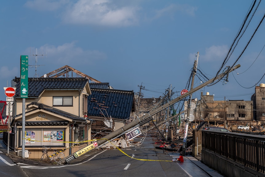 A road is pictured covered in debris, with fallen electricity poles blocking the way.