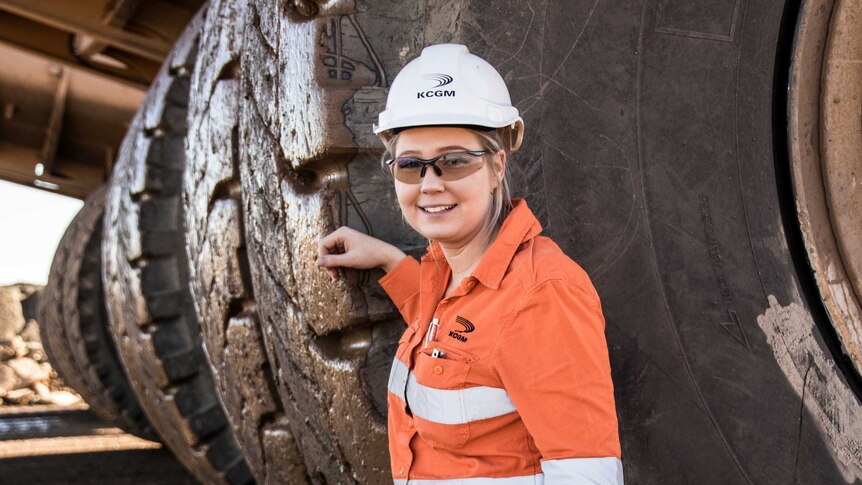 Woman standing next to tyre of big mining truck parked up