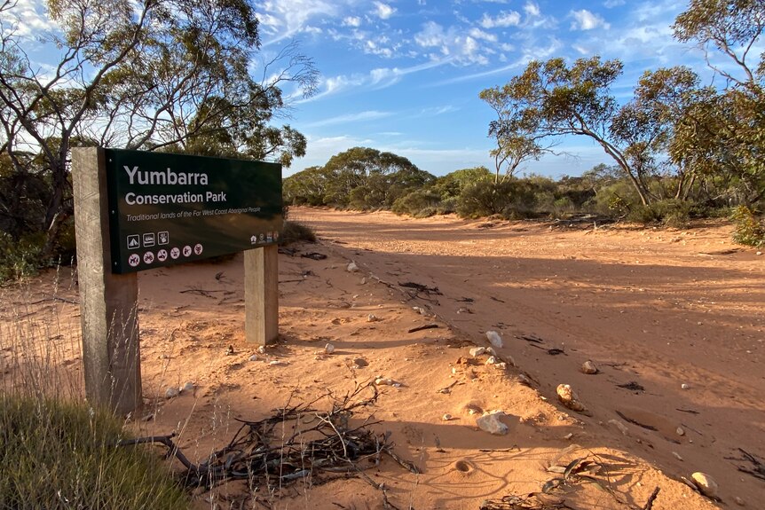 Yumbarra Conservation Park sign on dirt road edge, scrub in background