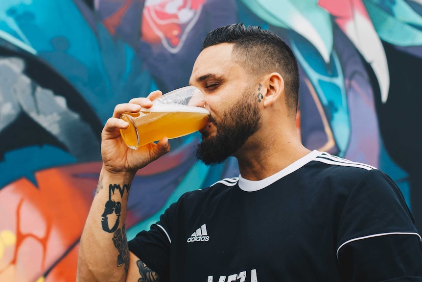 Man drinking beer from a glass in front of coloured background