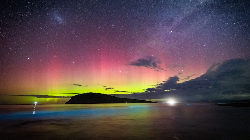 pink and yellow glow in the night sky, with blue glowing algae in the water