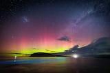 pink and yellow glow in the night sky, with blue glowing algae in the water