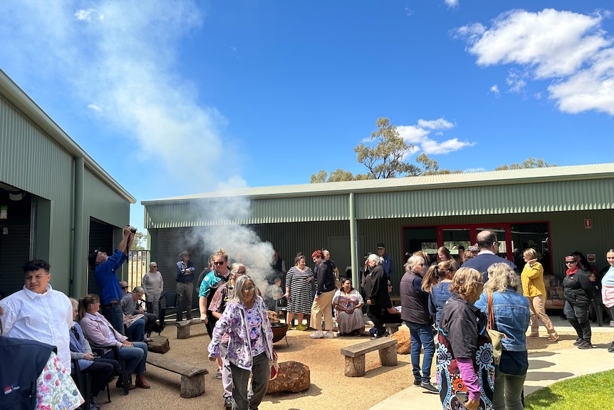 Dozens of people taking part in an indigenous smoking ceremony in a courtyard. 