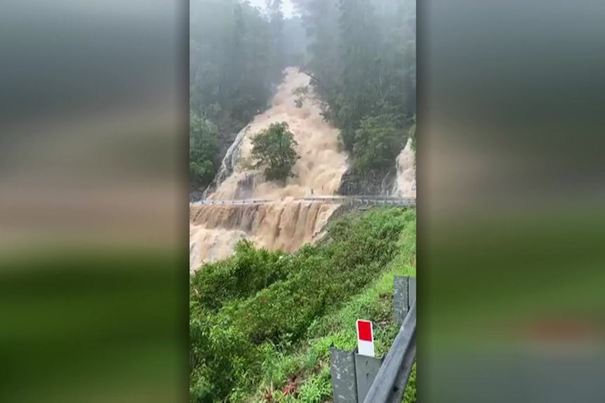 A large volume of water flowing down the side of a hill and over a road.