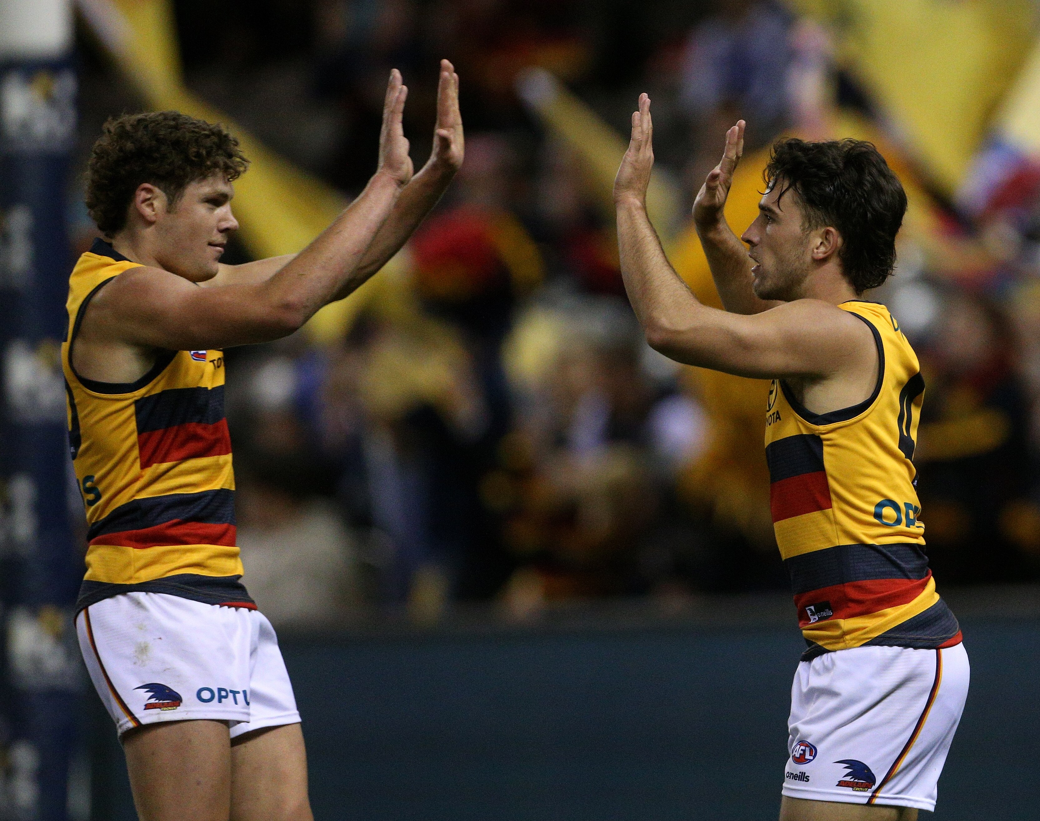 Two Adelaide Crows AFL players give each other a high five as they celebrate a goal.