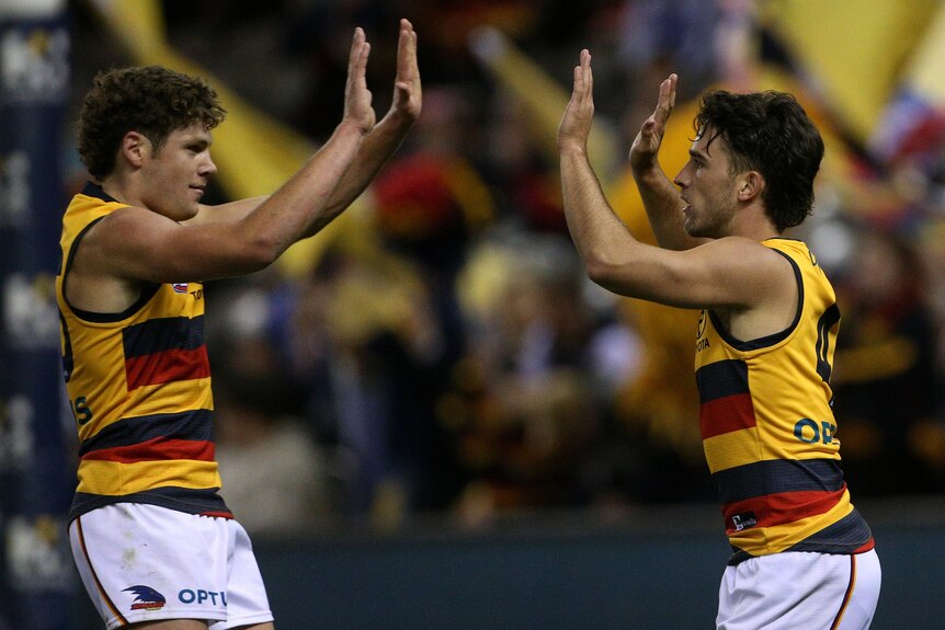 Two Adelaide Crows AFL players give each other a high five as they celebrate a goal.