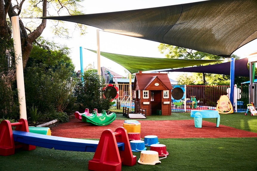 Colourful playground equipment and a brown cubby house under shade sails.