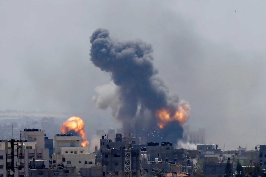 A large plume of smoke rises amid fireballs in a city landscape.