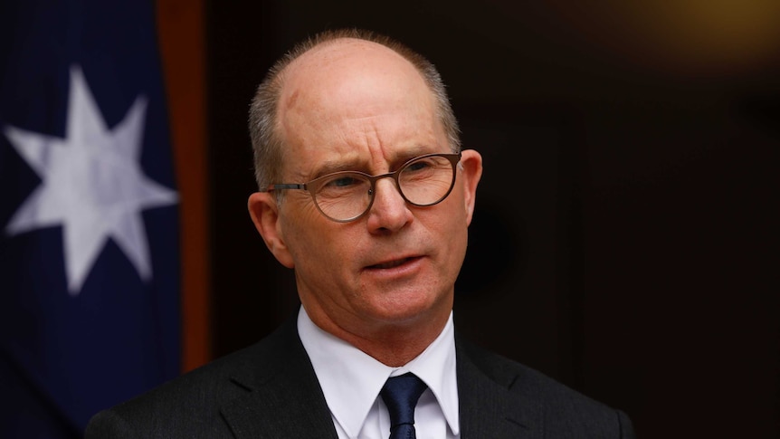 A portrait image of a balding man wearing glasses, a suit and a dark tie.