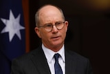 A portrait image of a balding man wearing glasses, a suit and a dark tie.