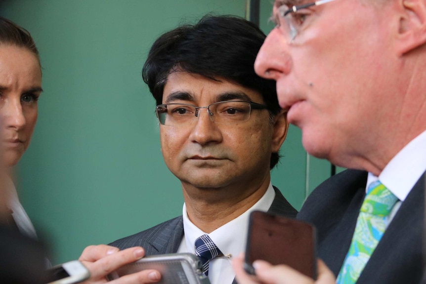 Lloyd Rayney looks stony-faced as his lawyer Martin Bennett speaks to reporters holding mobile phones and microphones.