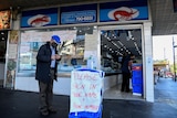 A shopper wearing a face mask signs into a seafood store before entering in Bankstown.