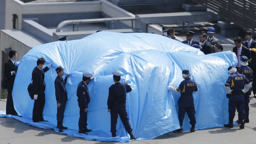 Police hold down a large blue tarp on a roof in Japan.