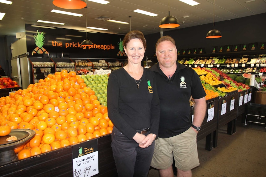 A woman and man stand in a fruit shop full of colourful fruit