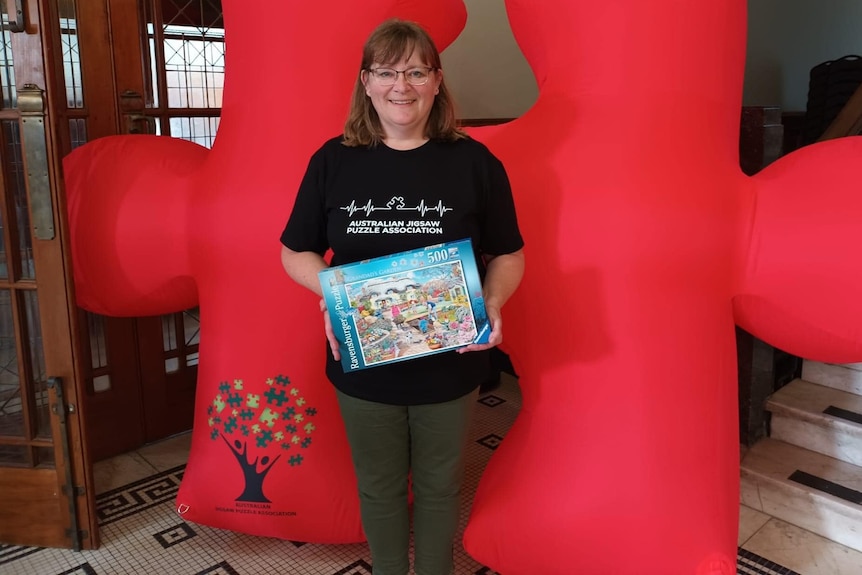 Woman holding puzzle box in front of inflatable puzzle piece.