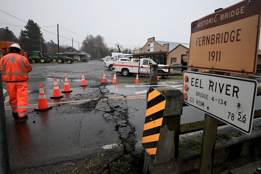 Traffic cones over a road with large cracks in it