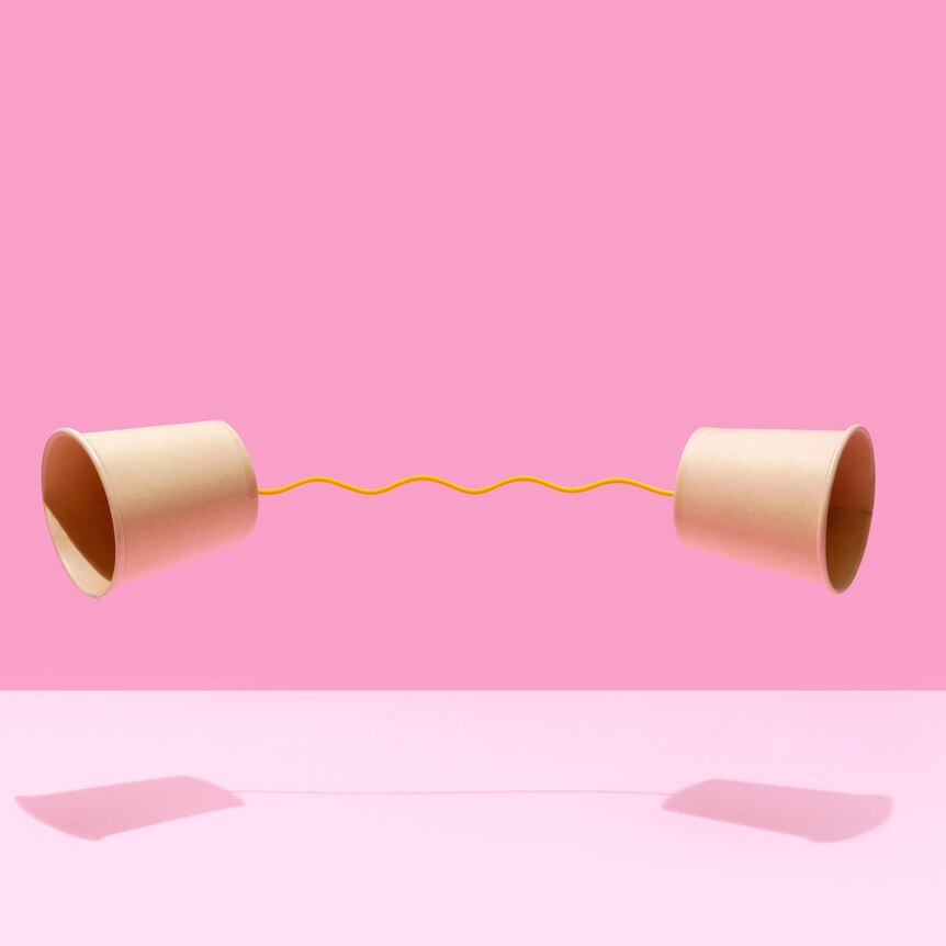 Two paper cups on a pink background. They are connected by yellow string at their bases. 