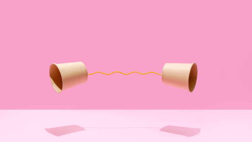 Two paper cups on a pink background. They are connected by yellow string at their bases. 
