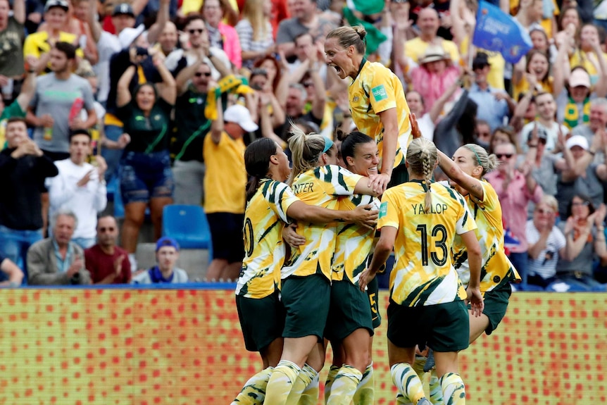 The Matildas huddle in celebration in front of a roaring crowd