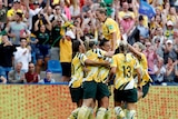 The Matildas huddle in celebration in front of a roaring crowd