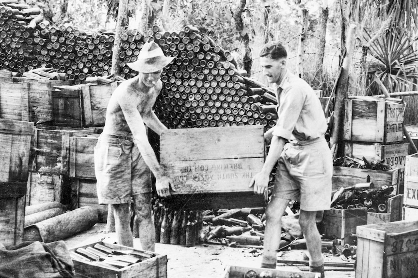 Monochrome of two defence members loading crates with empty beer bottles piled high.