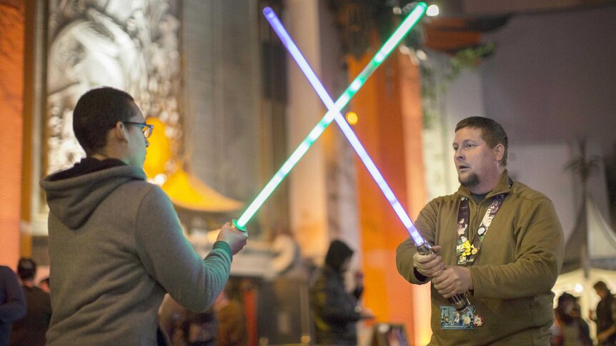 Two fans have a light saber fight as they wait in line for the premiere of Star Wars: The Force Awakens