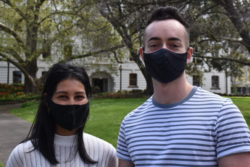Alannah Manuk and Kyle Jones, both wearing black face masks, smile as they stand in a park.