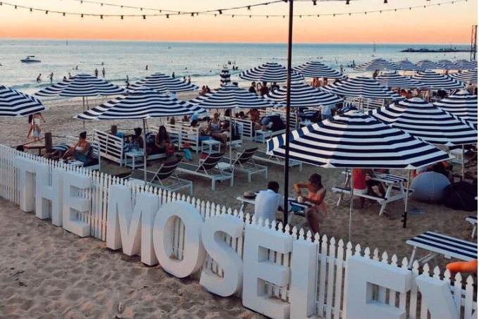 Tables and chairs with striped umbrella are set up on a beach at sunset
