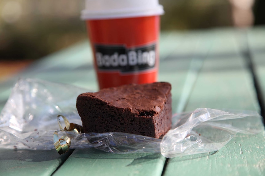 A chocolate brownie and takeaway coffee from Bada Bing, on a picnic table.