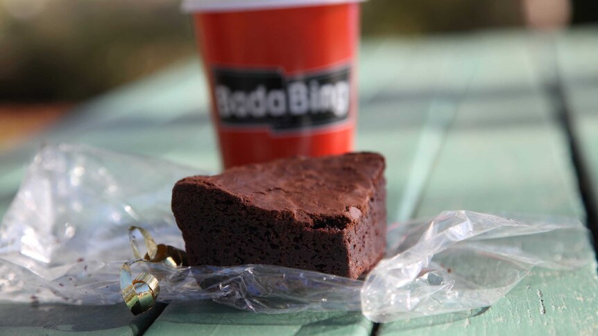 A chocolate brownie and takeaway coffee from Bada Bing, on a picnic table.