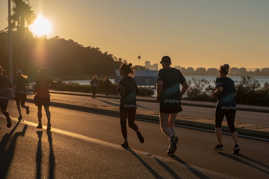 Dozens of people smile and wave while standing at the start line for the 2019 HBF Run for a Reason fun run in Perth.